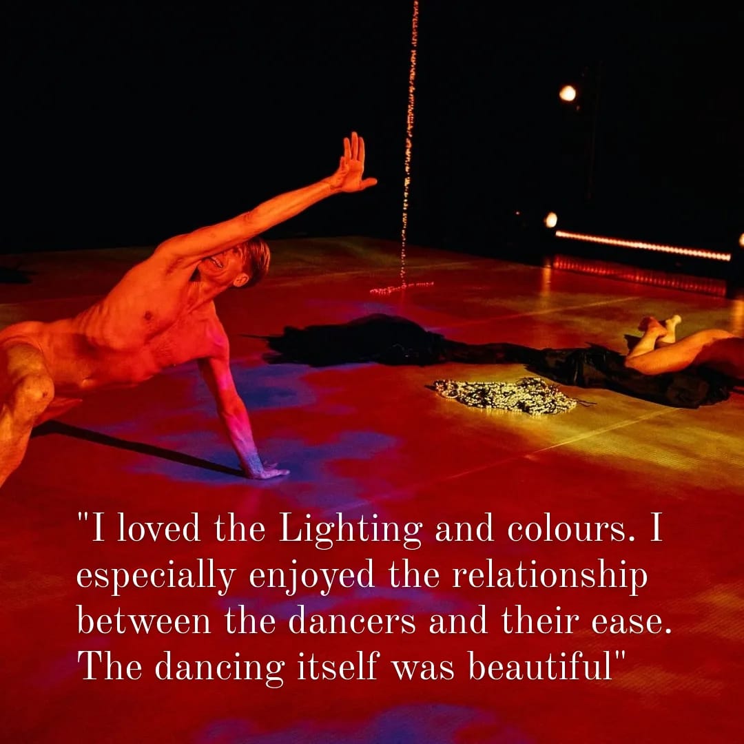 Two naked dancers bathed in red, purple and yellow projection. Both on the ground, one extended in a lunge, the other resting on a swathe of fabric. The text says: "I loved the lighting and colours. I especially enjoyed the relationship between the dancers and their ease. The dancing itself was beautiful".